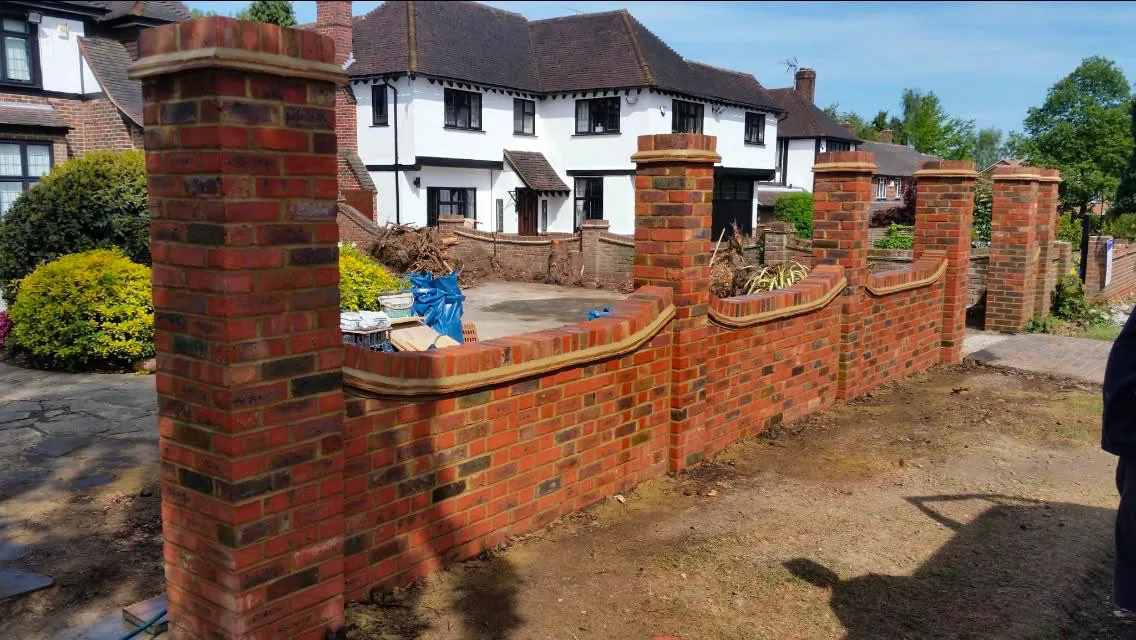 Before: the new brick boundary wall with its piers and shaped coping built, standing on bare dug-over ground with rubble still around it