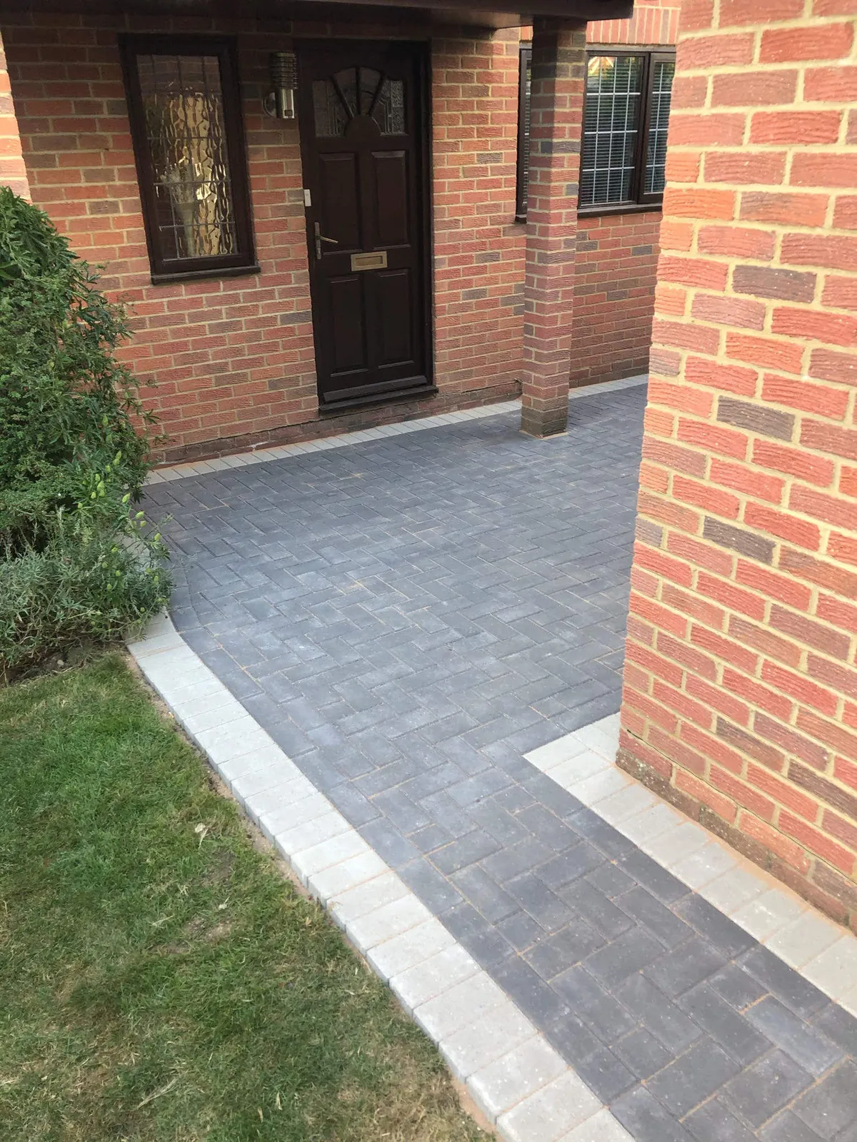 Front entrance path in grey herringbone paving with a light border between brick columns