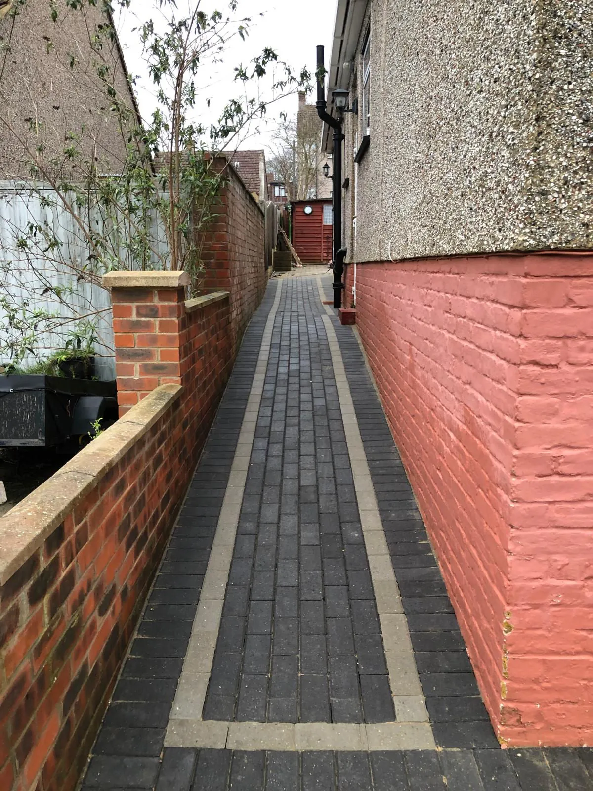 Narrow side return path in block paving with a light border stripe between painted and brick walls