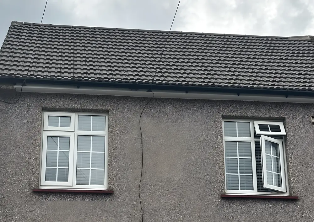 New fascia, soffit and guttering along the eaves of a pebbledashed house, under a new tiled roof
