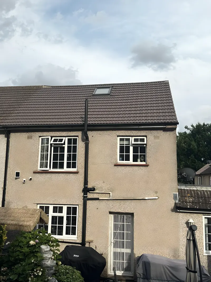 New fascia and black guttering along the eaves at the back of a pebbledashed house, with a rooflight in the tiled slope above