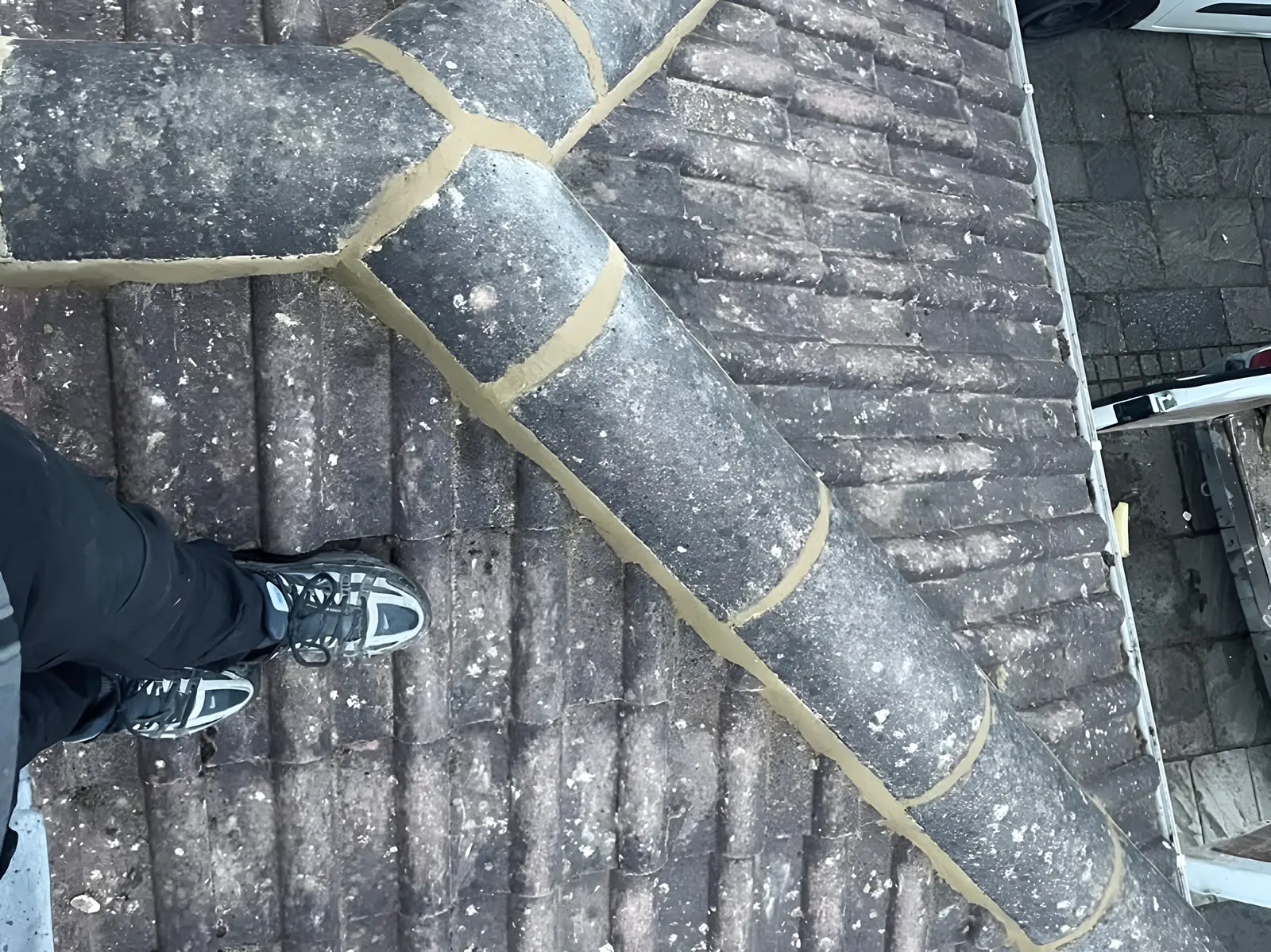 Hip tiles bedded and pointed in fresh mortar, seen from above, a roofer's feet on the tiles