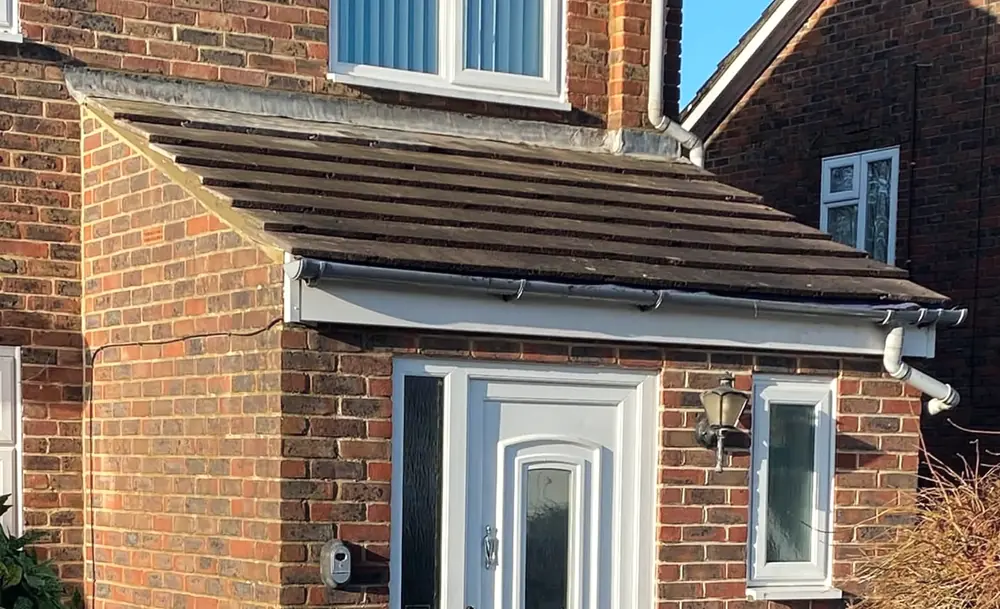 A porch roof over a front door with white fascia and guttering along its edge
