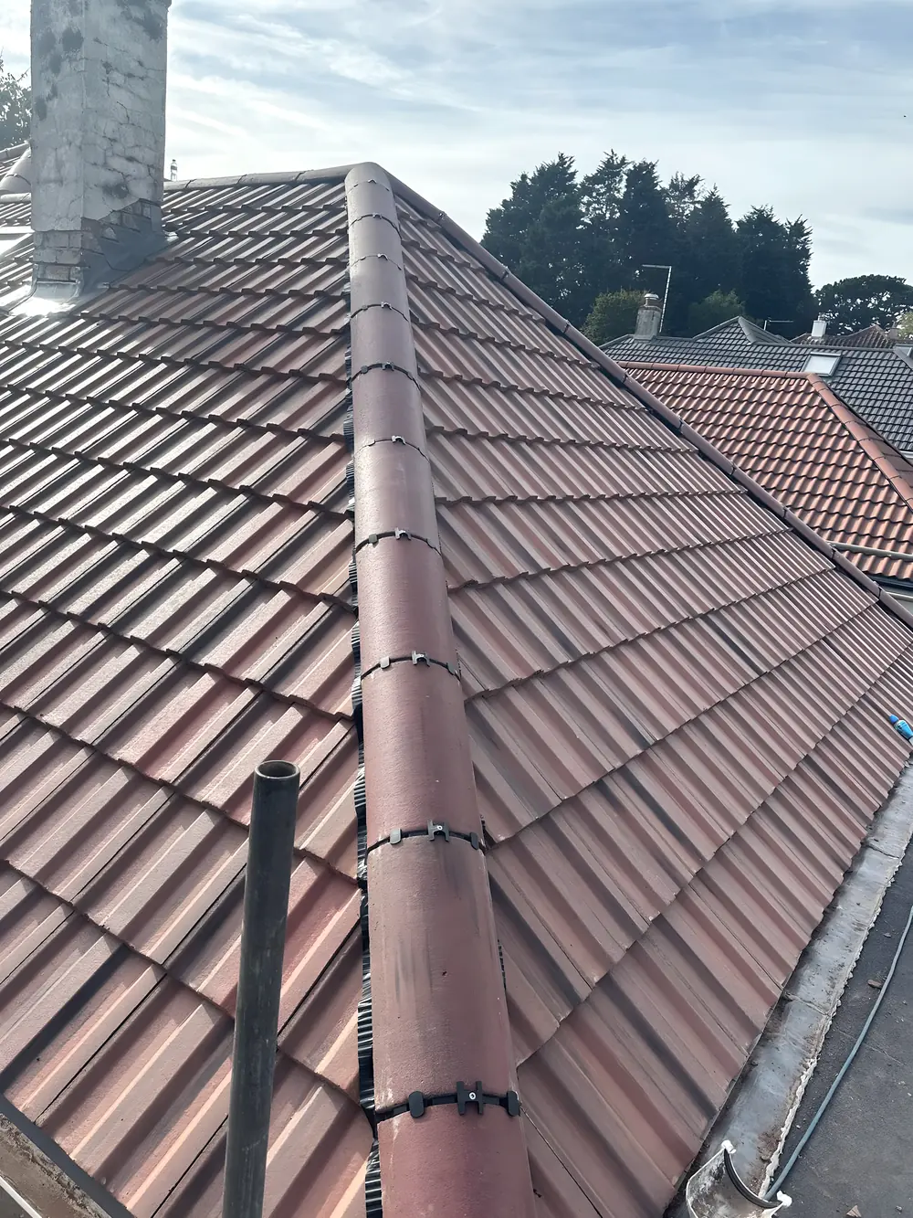 A red tiled roof of ours with the hip tiles clipped down along the hip line and a chimney stack at the top of the slope