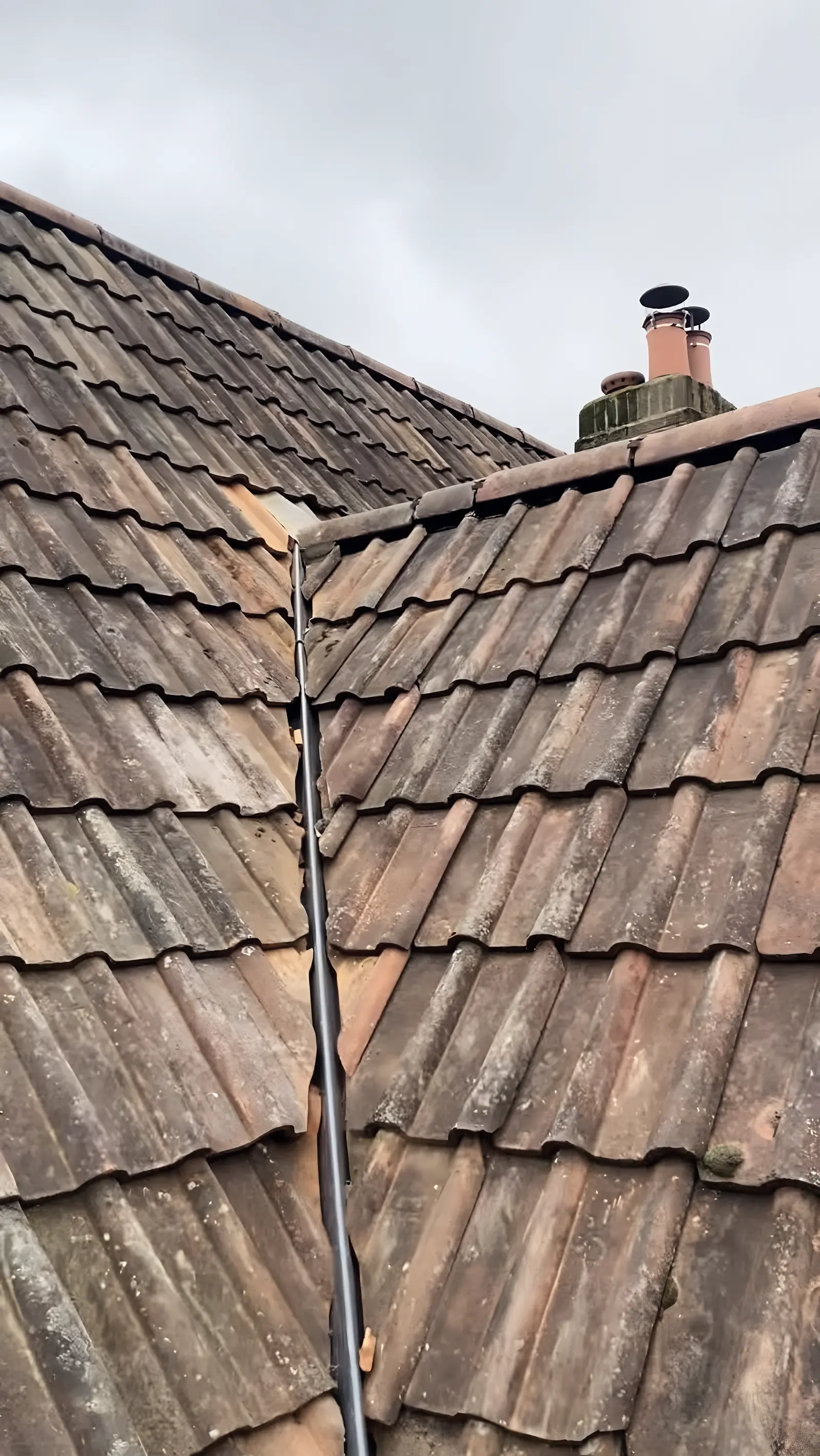 A valley between two tiled slopes with the tiles cut in neatly along both sides, a chimney with pots at the top