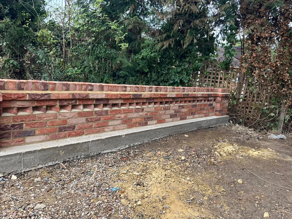New red brick retaining wall with a dentil course and brick on edge coping, built off a poured concrete footing with fresh hardcore in front