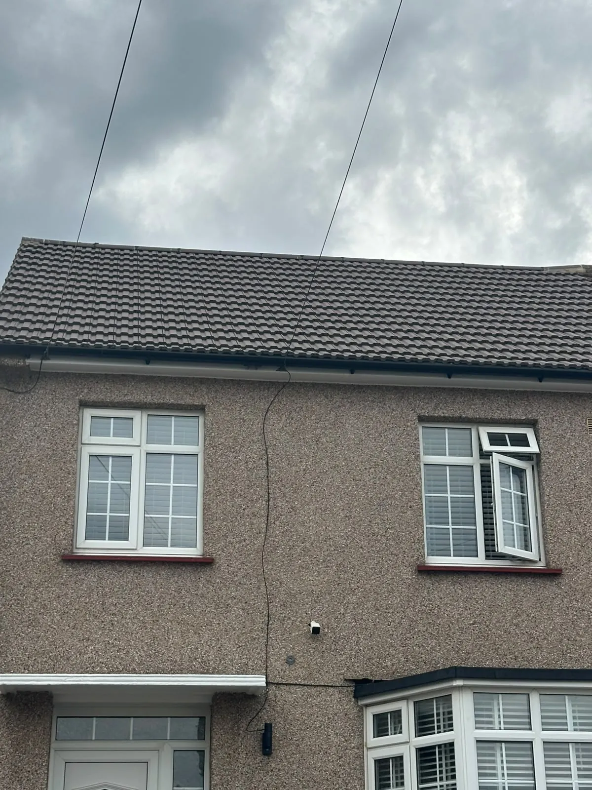 Finished brown tiled roof on a pebbledashed house, with new black fascia, soffit and guttering run along the eaves