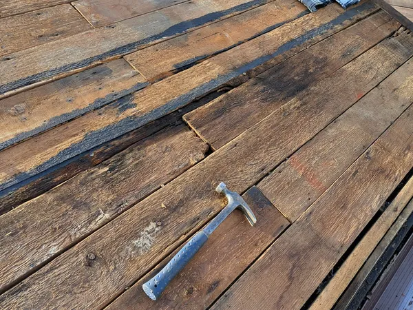 Old timber roof boards with the covering stripped off, black bitumen left along the joints and a hammer lying on the deck