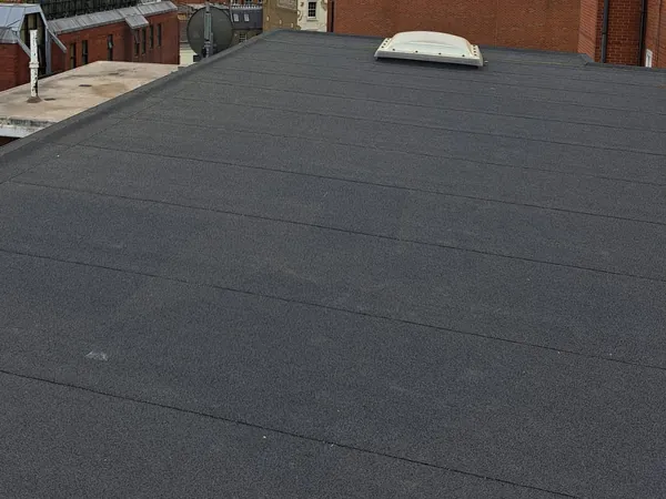 A large flat roof covered in black mineral felt laid in overlapping runs, with a domed rooflight and brick walls beyond