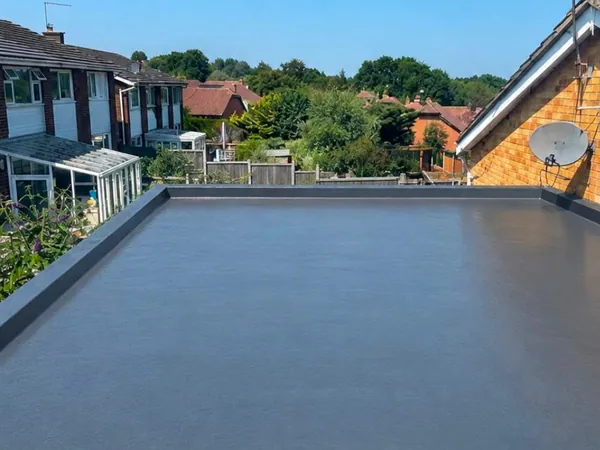 A finished flat roof in a smooth grey covering with raised edge trims, back gardens and houses beyond