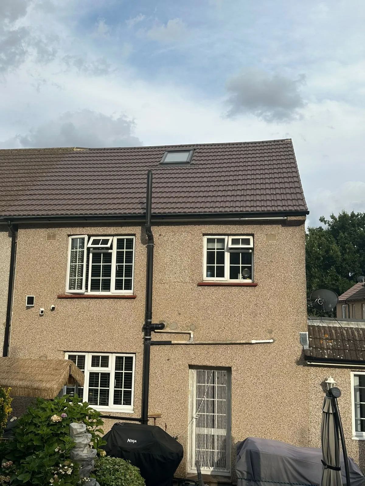 Finished brown tiled roof with a rooflight set into the slope and new black fascia, soffit and guttering, on the back of a pebbledashed house