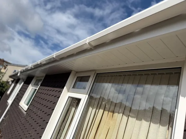 New white uPVC fascia, soffit and guttering along the eaves of a tile-hung house, over a big window