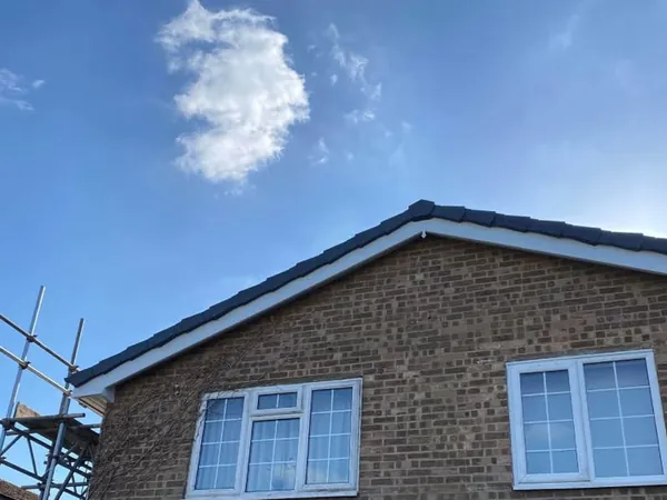 After: the same gable with new white boards and soffit, and dark verge caps along the edge of the tiles