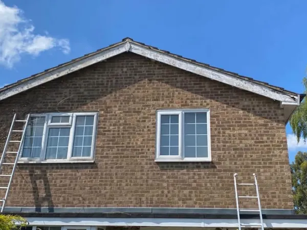Before: a brick gable with old, flaking white bargeboards and ladders against the wall