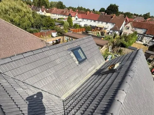 A finished grey tiled roof with a valley, a dry fixed ridge and a rooflight, houses and gardens beyond